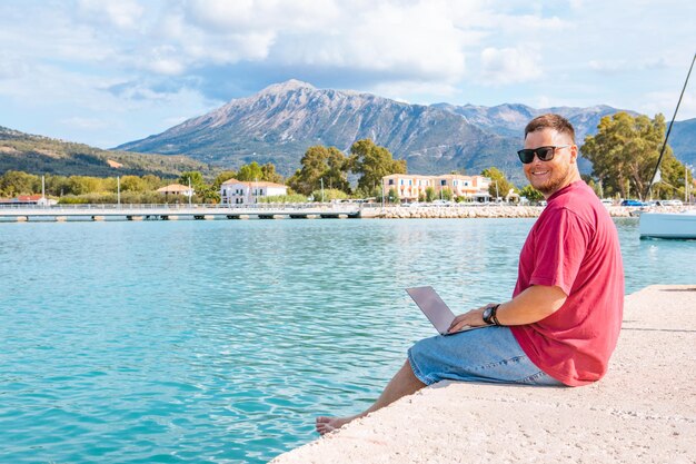 Freelancer hombre trabajando en un portátil en el verano del banco del puerto de la ciudad