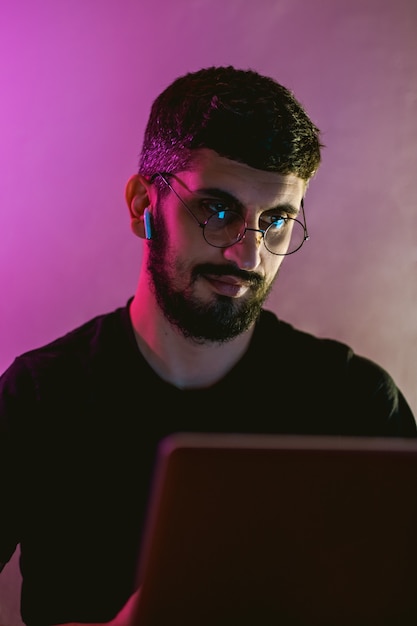 Freelancer jovem concentrado trabalhando em um laptop em uma sala com iluminação colorida.