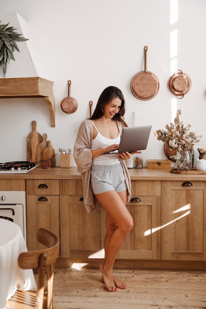 Freelancer jovem feliz na cozinha com um laptop nas mãos