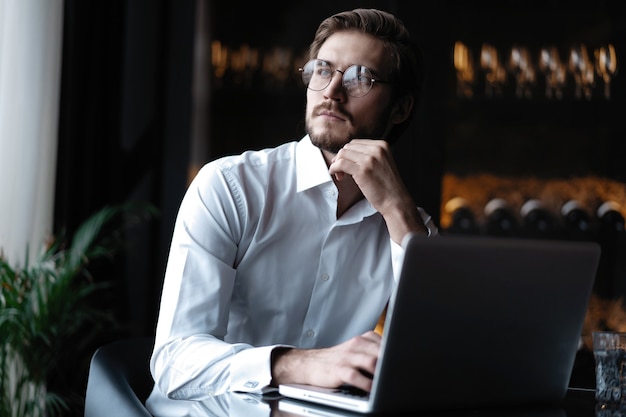 Freelancer joven y guapo está tomando un café y soñando después de trabajar con una computadora portátil en la cafetería.