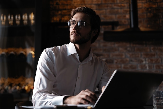 Freelancer joven y guapo está tomando un café y soñando después de trabajar con una computadora portátil en la cafetería.