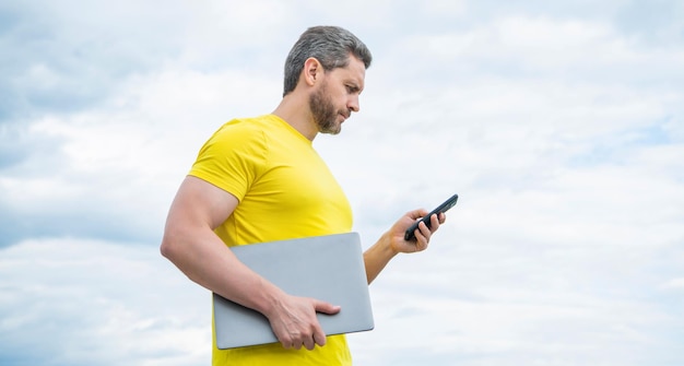 Freelancer con laptop chateando en smartphone sobre fondo de cielo