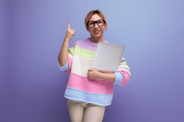 Freelancer loira bem-sucedida com um laptop nas mãos mostra espaço para cópia em um fundo roxo