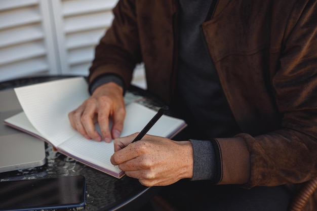 freelancer masculino escrevendo no caderno e tomando notas enquanto trabalhava no café urbano