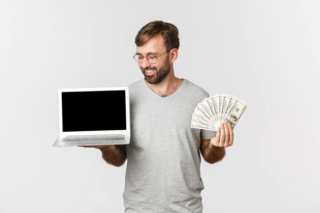 Freelancer masculino guapo mostrando dinero y pantalla de portátil