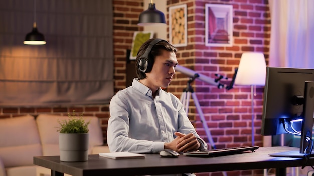 Freelancer masculino ouvindo aula de aula remota ou webinar de treinamento no computador para aprender o trabalho de negócios de inicialização. Usando o estudo de podcast com fones de ouvido sem fio para planejar o relatório do aplicativo.