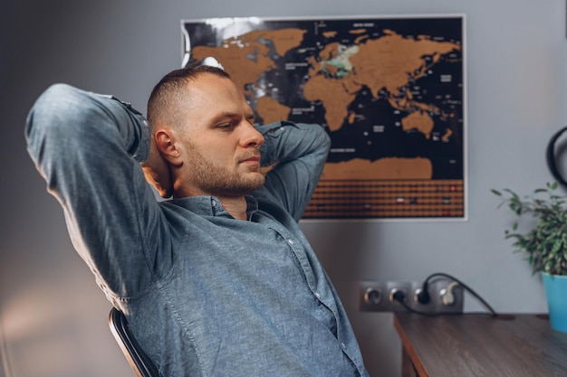 Freelancer masculino relajado descansando durante el trabajo remoto mientras se sienta con las manos detrás de la cabeza en casa