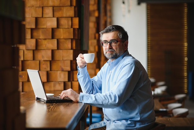 Freelancer masculino sênior trabalhando no laptop no conceito de trabalho remoto de café