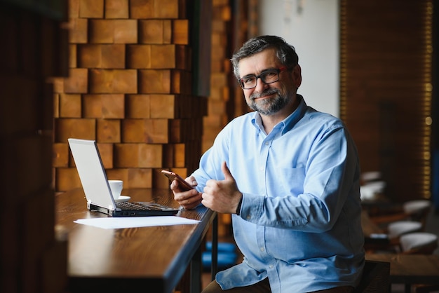 Freelancer masculino sênior trabalhando no laptop no conceito de trabalho remoto de café