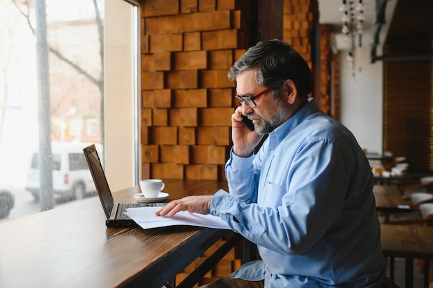 Freelancer masculino sênior trabalhando no laptop no conceito de trabalho remoto de café