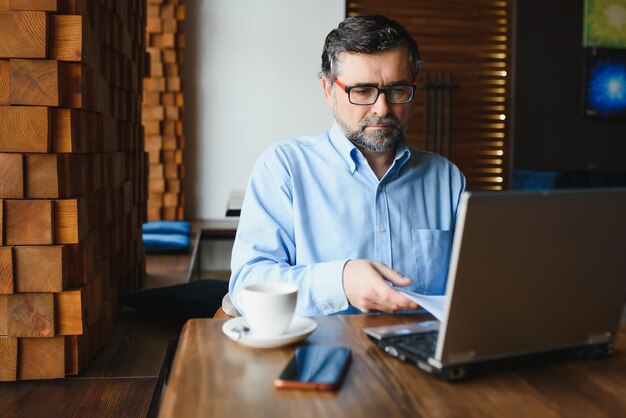 Foto freelancer masculino sênior trabalhando no laptop no conceito de trabalho remoto de café