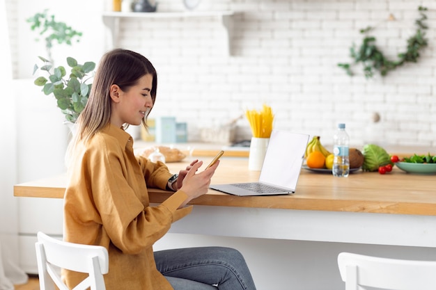 Freelancer mujer caucásica joven sentado en casa en la cocina trabajando de forma remota