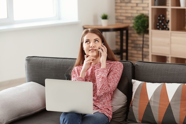 Freelancer mujer hablando por teléfono mientras trabaja en la computadora portátil en casa