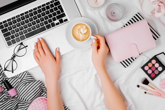 Freelancer de mujer joven que trabaja con la computadora portátil en la cama, endecha plana, vista superior