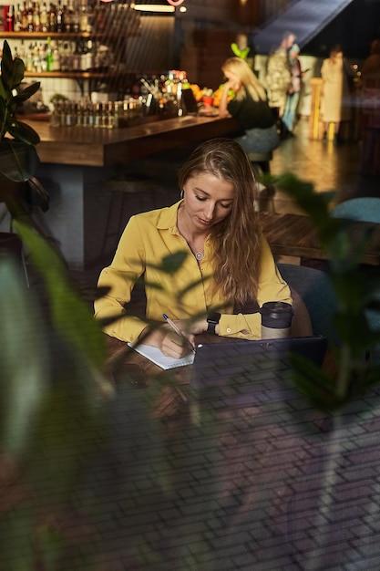 Freelancer mujer sentada en la mesa disparó a través del cristal de la ventana fuera del café