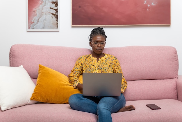 Freelancer de negocios negro concentrado trabajando en un proyecto de inicio y sentado en el sofá en la sala de estar