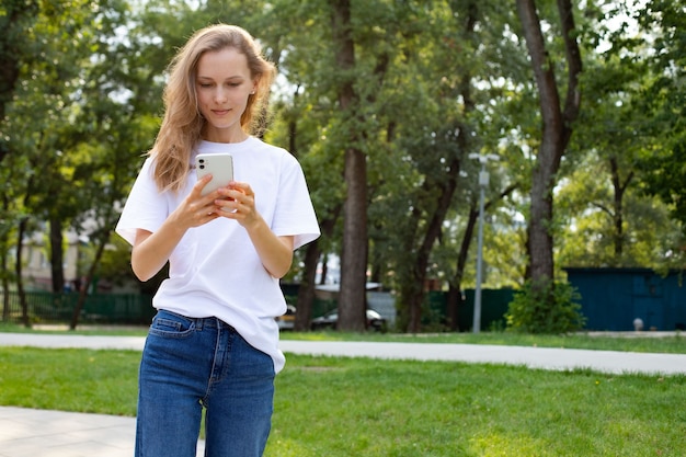 Freelancer pensativo mujer caucásica en ropa casual navegando por teléfono móvil mientras camina en el parque