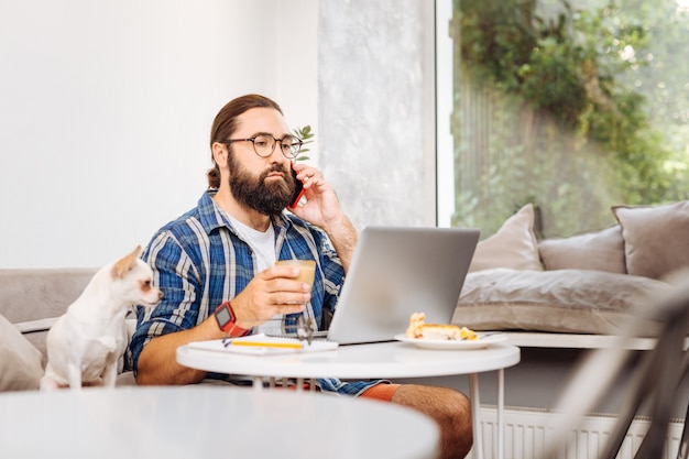 Freelancer próspero ocupado se sentindo relaxado enquanto bebe um pouco de café com leite trabalhando em um laptop