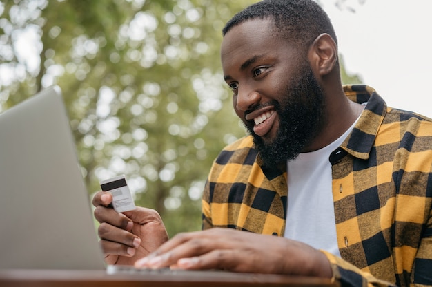 Freelancer recibe pago. Hombre afroamericano con tarjeta de crédito, usando laptop, compras en línea