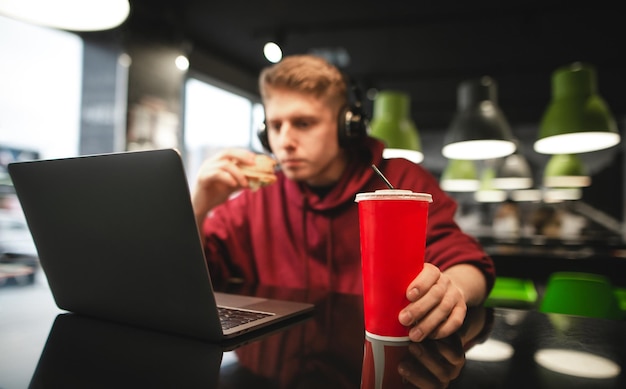 Freelancer trabaja en un restaurante de comida rápida y come una hamburguesa Concéntrese en el vaso rojo