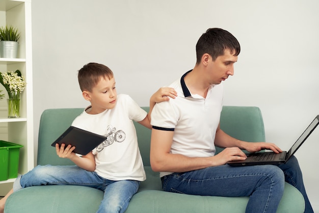 Freelancer trabajando en casa en condiciones confortables. Hombre tratando de trabajar, el niño impide que su padre trabaje.