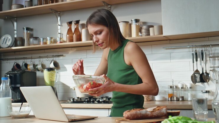 Foto freelancer trabajando en la cocina comiendo ensalada en casa mujer seria buscando portátil