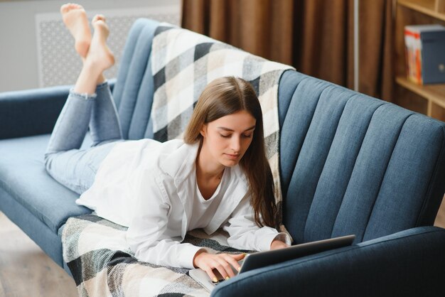 Freelancer trabajando en una computadora portátil en casa acostado en un cómodo sofá beige