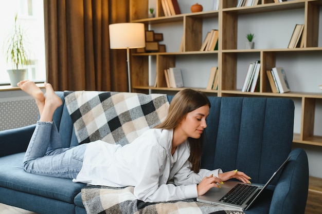 Freelancer trabajando en una computadora portátil en casa acostado en un cómodo sofá beige