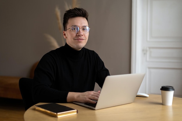 Freelancer um homem com óculos em roupas elegantes trabalha em um espaço de coworking usa um laptop