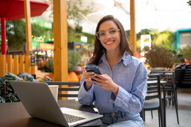 Freelancer usando smartphone e laptop sentado no café ao ar livre