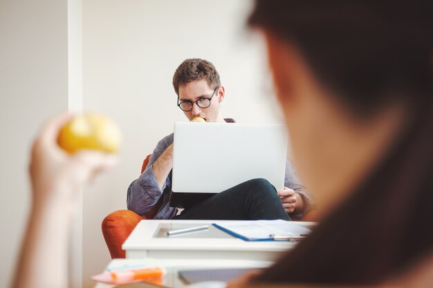 Freelancers que trabajan desde casa cerca de computadoras portátiles mientras comen manzanas Pareja sentada frente al baño del hombre ...