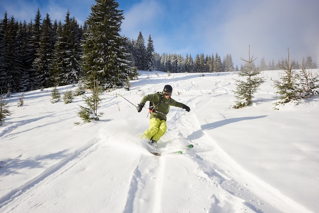Freeridender männlicher Skifahrer auf weit geöffneten Pisten in der Abfahrt. Skifahren zwischen Tannen. Extremes Aktivitätskonzept