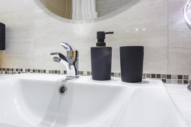Fregadero de agua de cerámica con grifo con dispensadores de jabón y champú negro en un baño caro