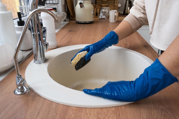 Fregadero de limpieza en la cocina antes de las vacaciones de Navidad y Año Nuevo Mano en guantes y esponja detergente polvo seco Decoración festiva en la cocina blanca acogedor interior de la casa