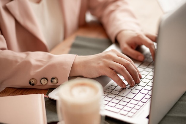 Freiberufler arbeitet an einem Computer in einem Café Mädchen Geschäftsfrau in einer beigefarbenen Jacke tippt auf der Tastatur Geschäftsessen Online-Meeting Geschäftskonzept selektiver Fokus