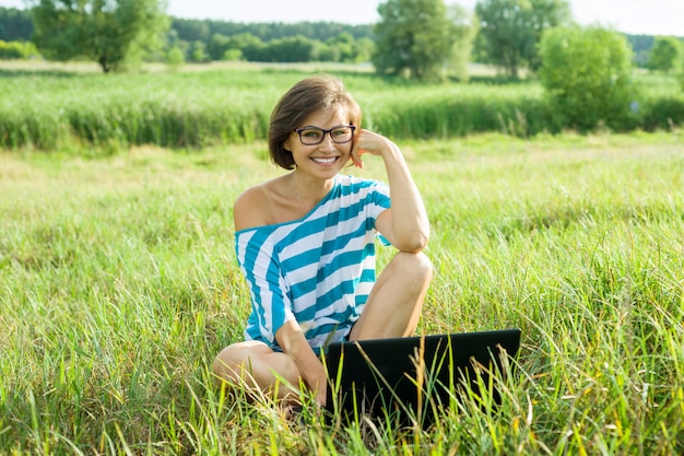 Freiberufler-Bloggerreisender der Frau von mittlerem Alter mit Laptop auf Natur