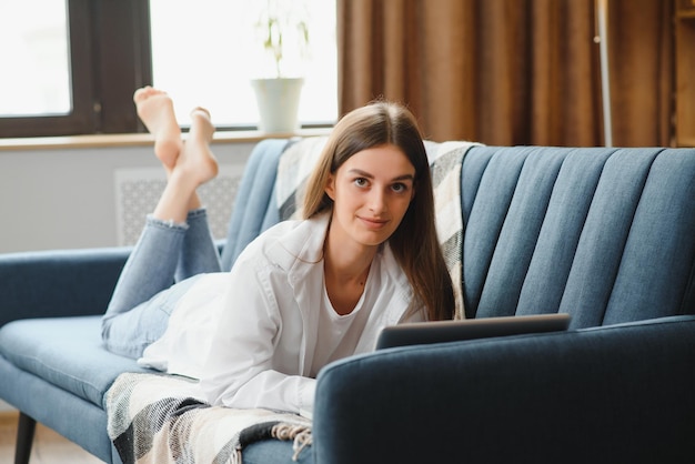 Freiberufler, der zu Hause am Laptop arbeitet und auf einem bequemen beigen Sofa liegt