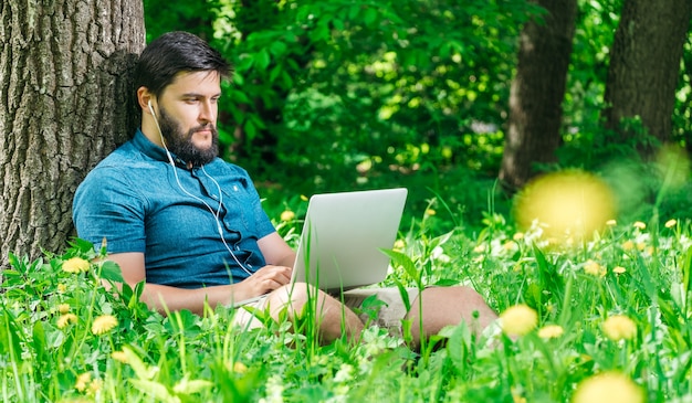 Freiberufler des jungen modernen Geschäftsmannes, der am Computer arbeitet und auf Gras sitzt