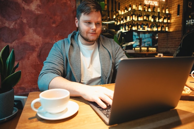 Freiberufler mit Headset, der im Café am Laptop arbeitet, Burger isst und Tee trinkt, Kopienraum