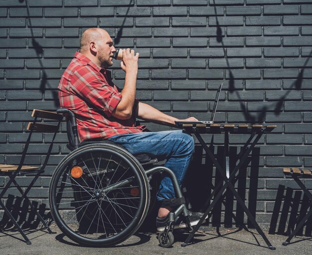 Foto freiberufler mit körperlicher behinderung, der im straßencafé im rollstuhl arbeitet