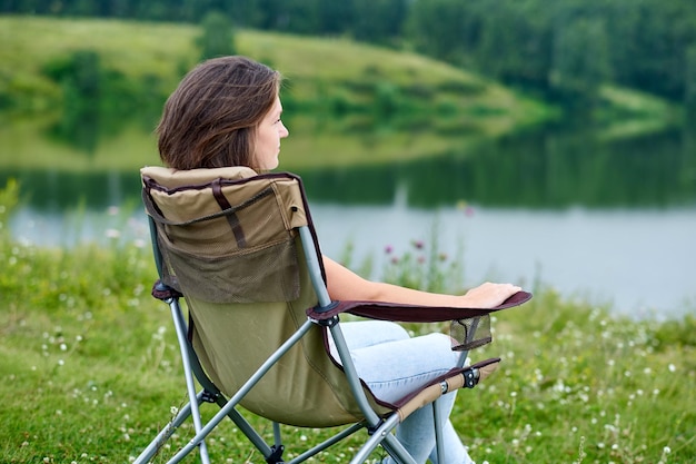 Freiberuflerin der jungen Frau, die auf einem Stuhl sitzt und sich in der Natur in der Nähe des Sees entspannt Outdoor-Aktivität im Sommer Abenteuerreisen im Nationalpark Freizeiturlaub Entspannung