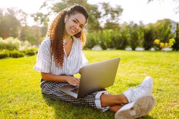 Freiberuflerin der jungen Frau, die auf grünem Gras mit Laptop sitzt Bildung online