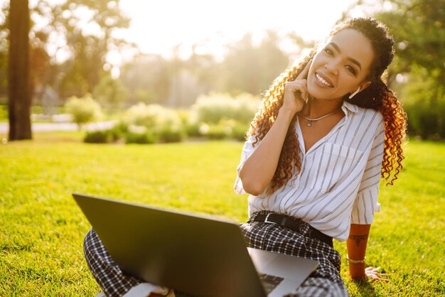 Freiberuflerin der jungen Frau, die auf grünem Gras mit Laptop sitzt Bildung online
