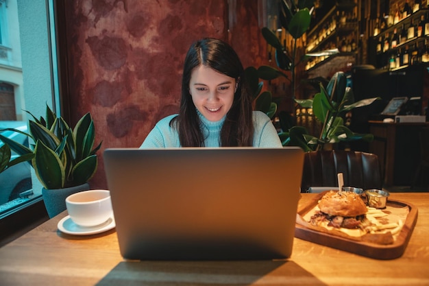 Freiberuflerin, die am Laptop im Café arbeitet und Tee trinkt, der Burger-Kopienraum isst