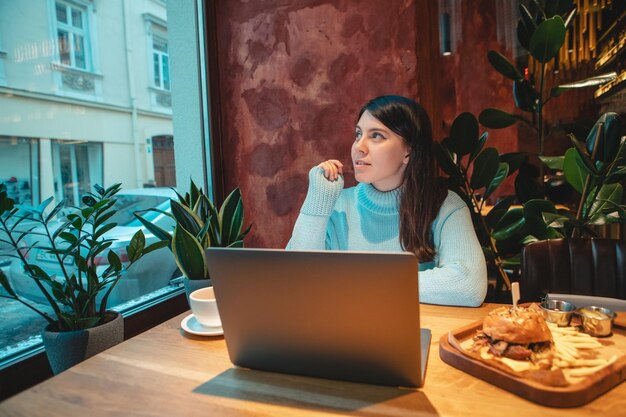 Freiberuflerin, die am Laptop im Café arbeitet und Tee trinkt, um Burgerkopienraum zu essen