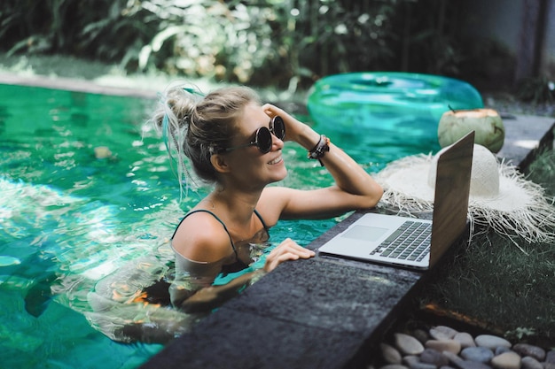 Freiberuflerin, die im Urlaub arbeitet. Junge Frau mit Laptop arbeitet, während sie auf einer Sonnenliege sitzt. Arbeiten Sie von überall, freiberuflich.