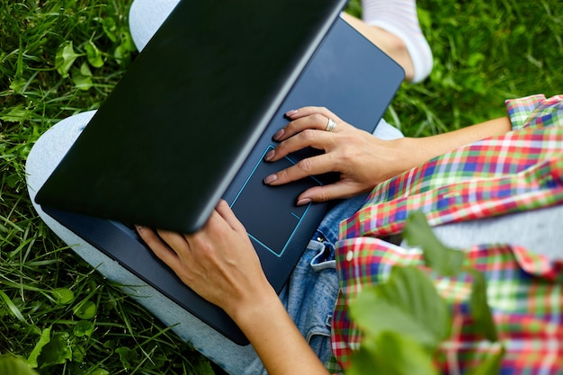 Freiberuflerin in Freizeitkleidung mit ihrem Computer-Laptop, die auf dem Gras im Park sitzt, freiberufliche Arbeit mit Notebook, intelligentes Büro im Freien, Mädchenstudium, Online-Bildung. Platz kopieren