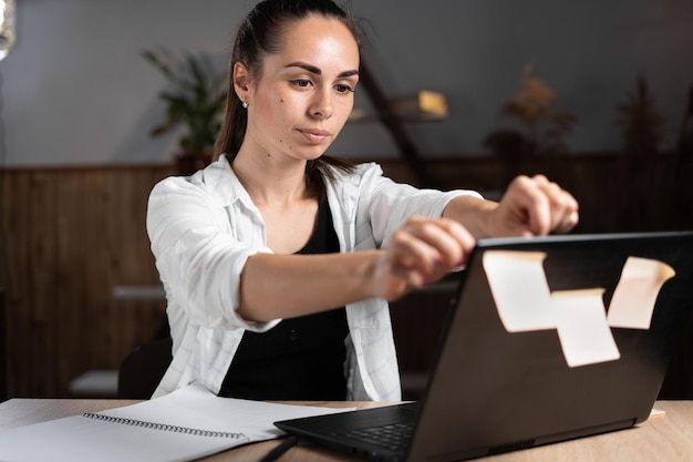 Freiberuflerin klebt klebrige Aufkleber auf einen Laptop, während sie an einem Home-Office-Tisch sitzt Mangel an Ideen und Schreiben auf Papier Geschäftsmannarbeit und Geschäftsfrauidee Kleinunternehmen