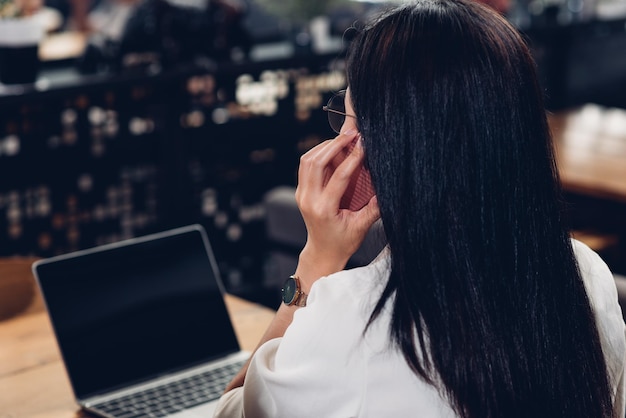 Freiberufliche berufstätige Frau mit Laptop-Computer, er ruft Smartphone mit Kunden im Café an