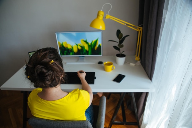 Freiberufliche Designerin, die zu Hause am Arbeitsplatz arbeitet, weißer Schreibtisch mit gelber Lampe